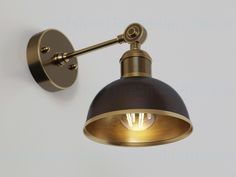 an antique brass wall light with a black and gold shade on the bulb, against a white background