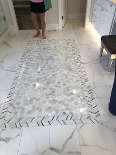 a woman is standing in the middle of a bathroom with white marble flooring and hexagonal tiles