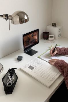 a woman sitting at a desk writing on a piece of paper next to a computer monitor