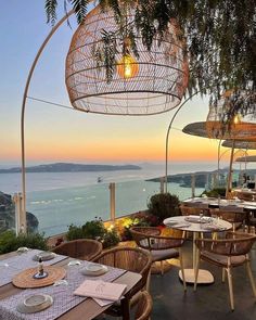 an outdoor dining area with tables and chairs overlooking the ocean at sunset or dawn,