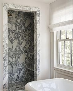 a bath tub sitting under a window next to a white sink in a room with marble walls and floors