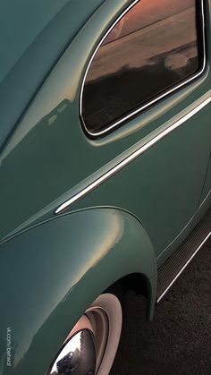 an old green car parked in a parking lot with the sun shining on it's side window