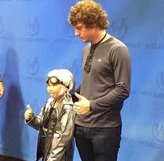 a young man standing next to a statue of a boy in a leather jacket and goggles