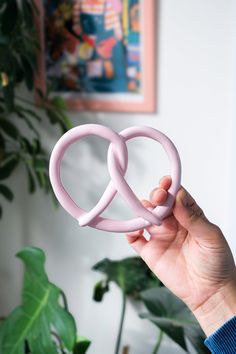 a person holding up two pink rings in front of a potted plant and painting on the wall