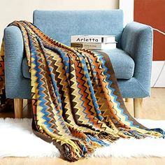 a couch with a blanket on top of it next to a book and a chair