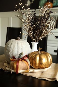 two pumpkins sitting on top of a wooden table next to a white vase filled with flowers