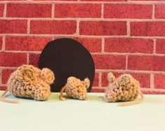 two crocheted mice sitting in front of a brick wall with a black circle