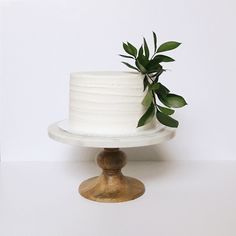 a white cake sitting on top of a wooden stand next to a green leafy plant