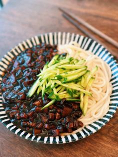 a plate filled with noodles and vegetables next to chopsticks on a wooden table