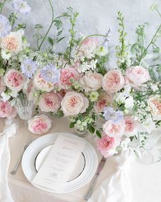 the table is set with pink and white flowers, silverware, and napkins