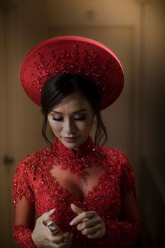 a woman in a red dress and hat looking down at her cell phone while holding something