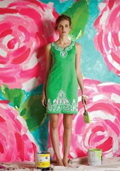 a woman standing in front of a wall with flowers painted on it and paint cans next to her