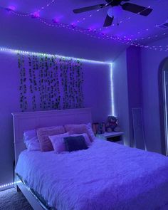 a bedroom with purple lights on the ceiling and a white bed covered in fluffy blankets