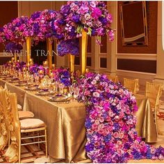 a long table covered in purple flowers and gold chairs