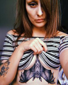 a woman with tattoos on her chest posing for the camera while wearing a striped shirt