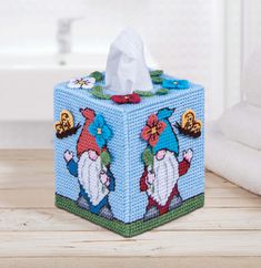 a blue tissue box with gnomes on it sitting on a wooden table next to a toilet paper roll