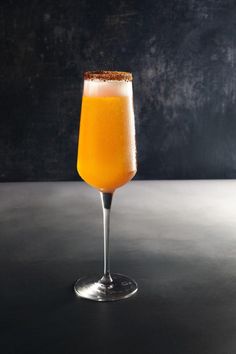 a glass filled with orange juice on top of a table next to a black wall