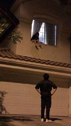 a person standing in front of a house with a dog hanging from the roof above them