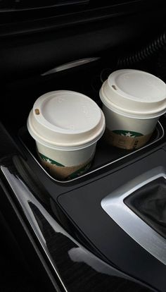 two coffee cups are sitting in the center console of a car, with their lids down