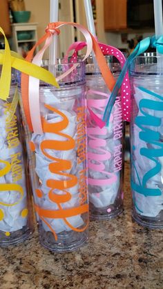 three personalized tumblers with ribbons on the handles are lined up next to each other