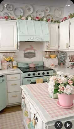 an old fashioned kitchen with pink and white flowers on the counter top, green cabinets