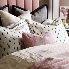 a bed with pink and black pillows on top of it next to a night stand