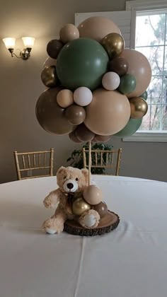 a teddy bear sitting on top of a table with balloons in the shape of animals