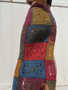 a crocheted skirt is hanging on the side of a white wall with a wooden fence in the background