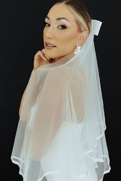 a woman wearing a white veil and posing with her hand on her chin, in front of a black background