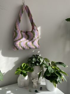 a crocheted bag hanging on the wall next to potted plants