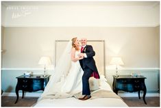 a bride and groom posing for a photo on the bed in their hotel room with two nightstands