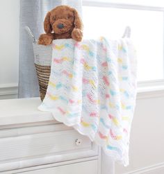 a teddy bear sitting on top of a blanket next to a basket and window sill