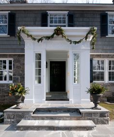 the front entrance to a house decorated with christmas wreaths and greenery on either side