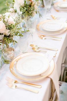 the table is set with white and gold plates, silverware, and floral centerpieces