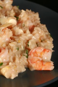 rice with shrimp and scallops is served on a black plate, ready to be eaten