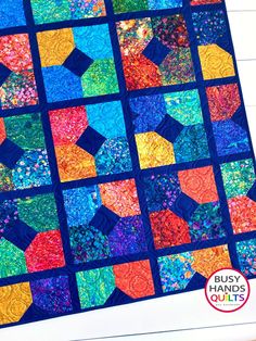 a colorful quilt is displayed on a white surface with the words busy hands quilts written below it