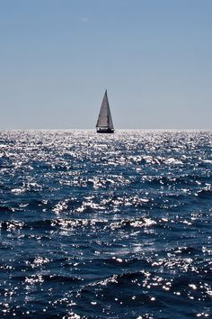 a sailboat is sailing in the middle of the ocean with bright blue skies above