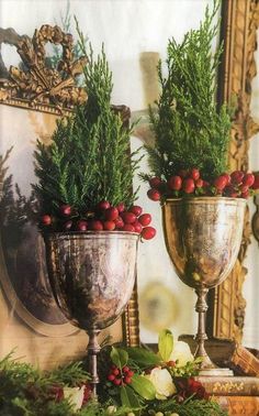 two silver goblets with red berries and greenery in them sitting on a mantle