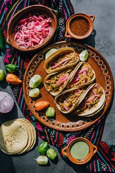 three tacos on a plate with salsa, limes, and other condiments