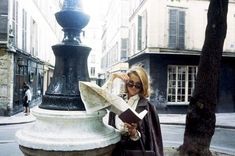 a woman is standing next to a lamp post and reading a book in the city