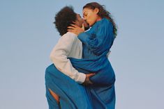 a man and woman kissing each other in front of a blue sky