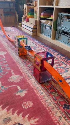 a toy train is laying on the floor in front of a rug and shelves filled with toys