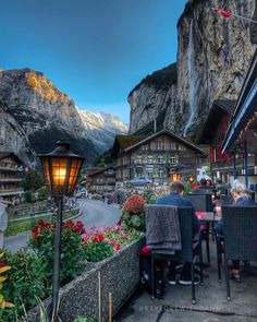 people are sitting at tables in front of the mountains and buildings with lights on them