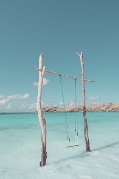 an empty swing in the middle of some blue water with two sticks sticking out of it