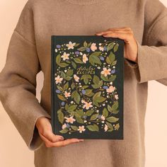 a person holding a book in their hands with flowers and leaves on the front cover