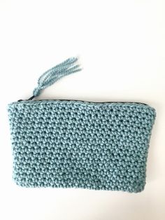 a crocheted blue purse with a tassel on the front and side, sitting on a white surface