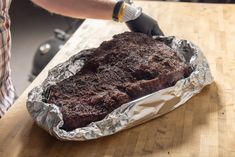 a person wearing gloves is cutting up a piece of food on a wooden table with aluminum foil