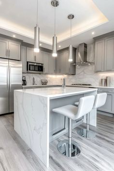 a kitchen with marble counter tops and white stools in front of an island that's surrounded by stainless steel appliances