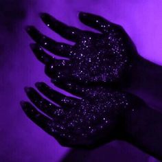 two hands with black glitter on them against a purple background