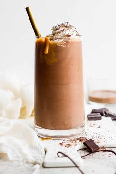 a glass filled with chocolate milkshake on top of a white table next to spoons